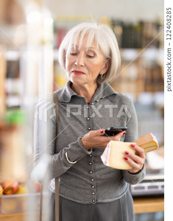 Mature female buyer scans QR code on cheese label in grocery store Mature female buyer scans QR code on cheese label in grocery store 122408285