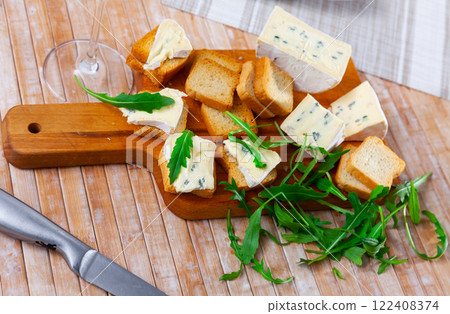 On table there is cutting board with blue cheese and hardtack decorated with arugula 122408374
