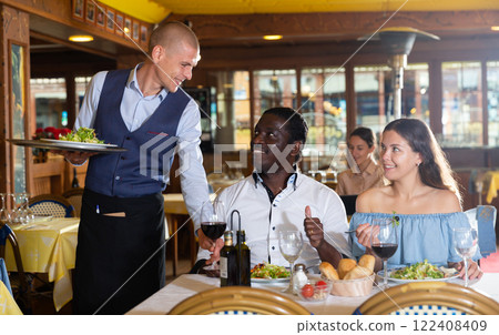 Male waiter writing down order from visitors in restaurant 122408409