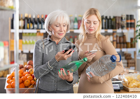 Elderly mother and her adult daughter scan a QR code on a bottles water label together to check expiration date 122408410