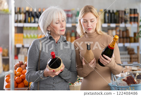 Shopping in produce supermarket - two female buyer makes choice bottle of wine Shopping in produce supermarket - two female buyer makes choice bottle of wine 122408486