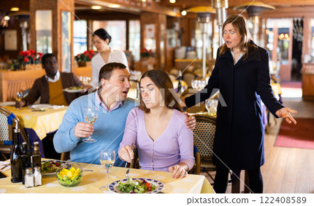 Resentful wife scolding her husband spending time with another woman at dinner Resentful wife scolding her husband spending time with another woman at dinner 122408589