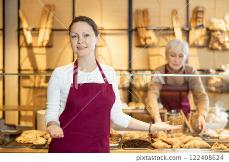 Positive middle-aged female business owner in apron standing in front of pastry stand in bakery shop. Concept of small local business 122408624