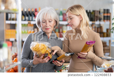 Girl and grandmother buyers examine good, doubt and choose pasta in store Girl and grandmother buyers examine good, doubt and choose pasta in store 122408653