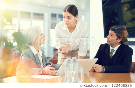 three positive office workers are sitting at table animatedly and actively discussing current work three positive office workers are sitting at table animatedly and actively discussing current work 122408826