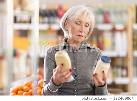 Choose food in supermarket - woman chooses mayonnaise to buy in the grocery department section of store 122409004