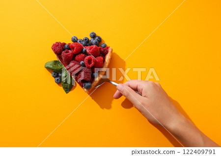 Piece of berry pie, berries, basil leaves and female hand on yellow background, top view 122409791