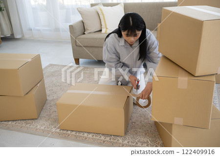 Young woman packing cardboard boxes for moving Young woman packing cardboard boxes for moving 122409916