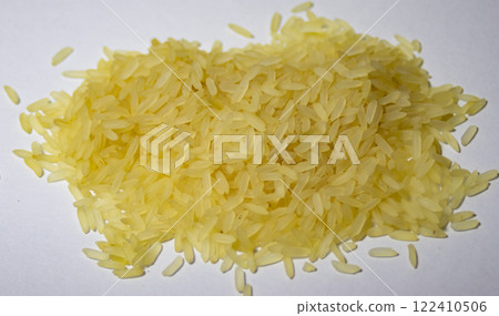 Very close-up photo of a pile of yellow parboiled rice on white background.  122410506