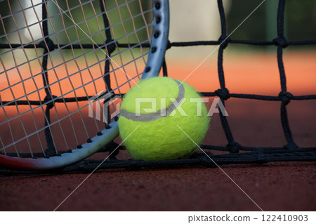 Tennis ball and racket leaning on the net of a clay court 122410903