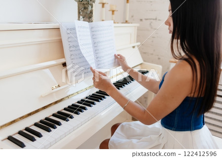 Woman sits at the piano and plays, reading from a sheet of music 122412596