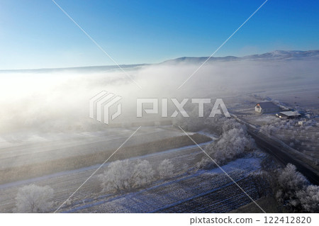 Aerial view of snow-covered landscape with fog rolling over fields and hills in winter season 122412820