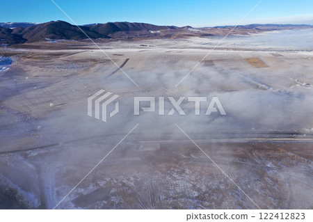 Aerial view of snow-covered landscape with fog rolling over fields and hills in winter season 122412823