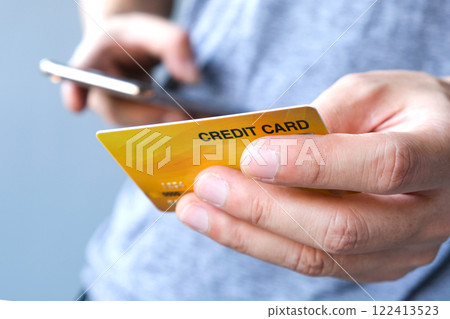 Young man sat in the living room on the sofa holding his credit card. Young man sat in the living room on the sofa holding his credit card. 122413523
