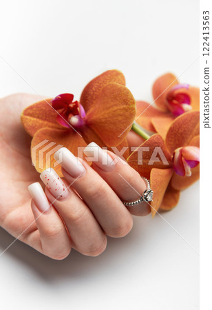 Woman hand showing stylish trendy nude manicure holding orange orchid flowers 122413563