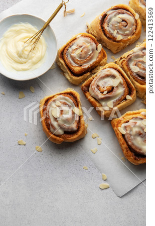 Freshly baked cinnamon rolls topped with cream cheese frosting and almond slivers 122413569