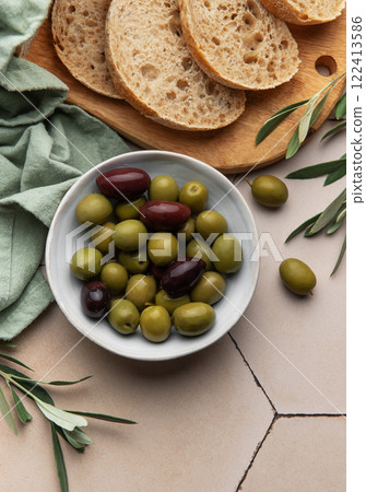 Sliced loaf of bread with green and black olives in a bowl on kitchen table 122413586