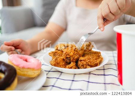 A woman is happily eating fried chicken and donuts on a plate. Fast food, Unhealthy food concept. A woman is happily eating fried chicken and donuts on a plate. Fast food, Unhealthy food concept. 122413804