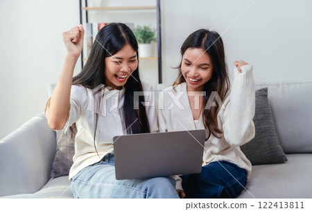 Two women are looking at a laptop screen and raising their arms in a gesture of joy and happiness Two women are looking at a laptop screen and raising their arms in a gesture of joy and happiness 122413811