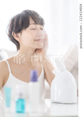 一位中年婦女用蒸臉器進行蒸氣清潔 一位中年婦女用蒸臉器進行蒸氣清潔 122414604