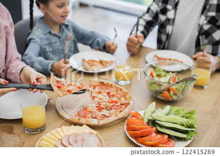 Caucasian family including young girl enjoying breakfast with pizza, salad, and orange juice. Relaxed morning gathering around dining table highlighting family togetherness and casual dining at home. Caucasian family including young girl enjoying breakfast with pizza, salad, and orange juice. Relaxed morning gathering around dining table highlighting family togetherness and casual dining at home. 122415269