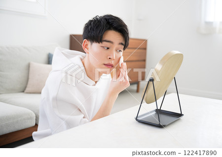 A top view of a young man looking in the mirror and applying makeup primer and foundation 122417890