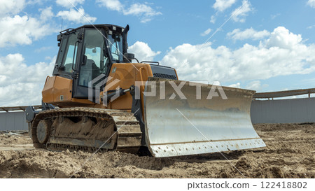 an orange bulldozer stands on a construction site with a lowered knife 122418802