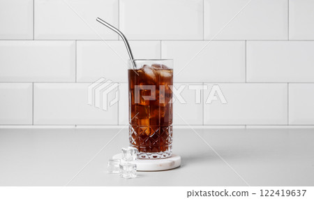 Cold brew coffee in a glass with ice and straw on a light table against a white brick background. 122419637