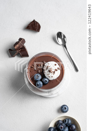 Chocolate pudding in a glass with whipped cream and fresh blueberry on a light background 122419643