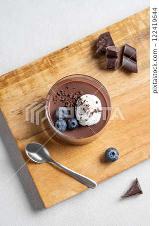 Chocolate pudding in a glass with whipped cream and fresh blueberry on a wooden board  122419644