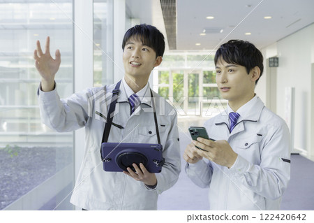 Two young men wearing work clothes having a conversation in an aisle Two young men wearing work clothes having a conversation in an aisle 122420642