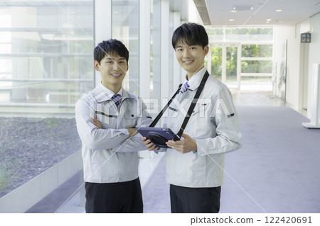 Portrait of two young men wearing work clothes and holding tablets standing in an aisle 122420691