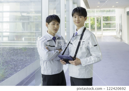 Portrait of two young men wearing work clothes and holding tablets standing in an aisle Portrait of two young men wearing work clothes and holding tablets standing in an aisle 122420692