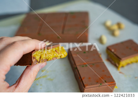 Piece of trend Dubai chocolate with pistachio paste and kataifi dough in woman hand. Confectionery handmade sweets at home in the kitchen.  122421033
