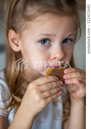 Little girl eating Dubai chocolate with pistachio paste and kataifi dough. Confectionery handmade sweets at home in the kitchen. Little girl eating Dubai chocolate with pistachio paste and kataifi dough. Confectionery handmade sweets at home in the kitchen. 122421042
