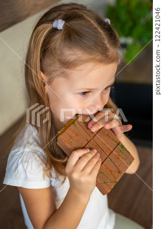 Little girl eating Dubai chocolate with pistachio paste and kataifi dough. Confectionery handmade sweets at home in the kitchen. Little girl eating Dubai chocolate with pistachio paste and kataifi dough. Confectionery handmade sweets at home in the kitchen. 122421046
