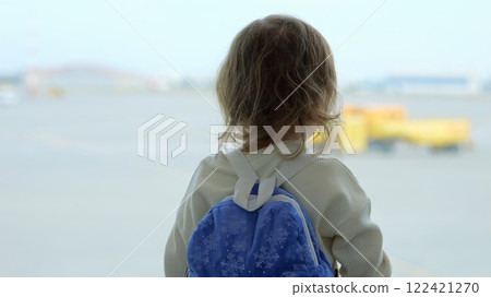 Preschooler girl waves hands looking at large airfield through window Preschooler girl waves hands looking at large airfield through window 122421270