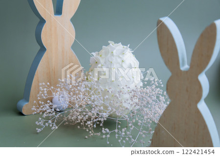 Wooden minimalism low-key bunny decor. Easter egg made of white lilac spring flowers in pastel green background. Sustainable holiday minimalistic still life composition. Copy space template for Wooden minimalism low-key bunny decor. Easter egg made of white lilac spring flowers in pastel green background. Sustainable holiday minimalistic still life composition. Copy space template for 122421454