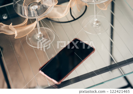 A modern mobile phone with an empty screen on the background of a transparent glass table. A smartphone with a black screen on the background of glasses. High quality photo A modern mobile phone with an empty screen on the background of a transparent glass table. A smartphone with a black screen on the background of glasses. High quality photo 122421465
