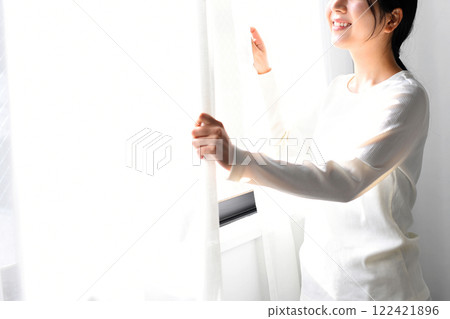 Asian woman opening the curtains and basking in the sunlight Asian woman opening the curtains and basking in the sunlight 122421896