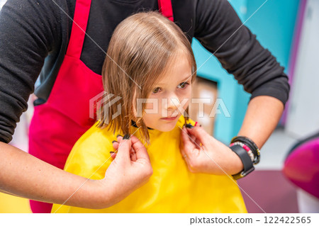 Close up view of hairdresser hands making a hair style to cute little girl in real child salon with colorful interior and toys Close up view of hairdresser hands making a hair style to cute little girl in real child salon with colorful interior and toys 122422565