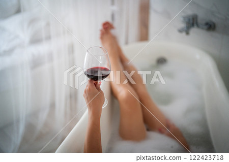 Close up of a woman holding glass of red wine in bathtub 122423718