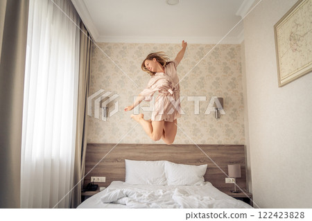Woman having fun and jumping with bathrobe on bed in hotel room 122423828