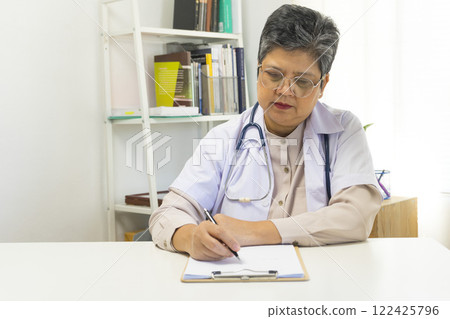 Asian doctor woman using a laptop computer and writing something on clipboard at hospital desk office, Healthcare medical concept. Asian doctor woman using a laptop computer and writing something on clipboard at hospital desk office, Healthcare medical concept. 122425796