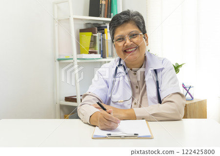 Asian doctor woman using a laptop computer and writing something on clipboard at hospital desk office, Healthcare medical concept. 122425800