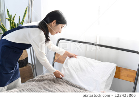 A woman in an apron making a bed 122425806
