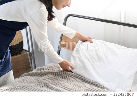 A woman in an apron making a bed 122425807