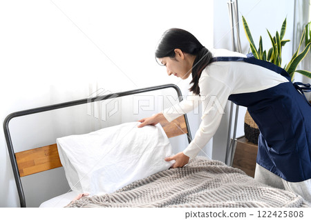 A woman in an apron making a bed 122425808