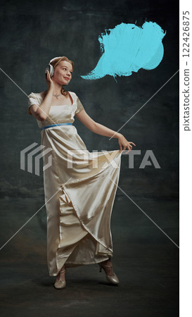 Portrait of elegant beautiful young woman in silk dress, royal person listening to music in headphones with blue speech bubble against dark vintage green background. Portrait of elegant beautiful young woman in silk dress, royal person listening to music in headphones with blue speech bubble against dark vintage green background. 122426875