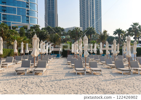 Rows of sun loungers for tourists are displayed against the backdrop of a luxury multi-story hotel Rows of sun loungers for tourists are displayed against the backdrop of a luxury multi-story hotel 122426902
